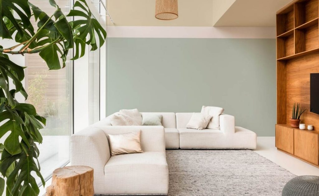 Soggiorno con divano angolare bianco, parete verde menta e mobili in legno scuro.