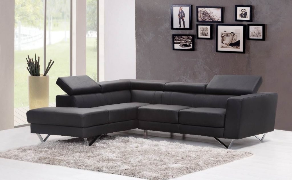 Divano in pelle nero con tappeto peloso di colore grigio. Quadri con cornice nera su parete grigio scuro.