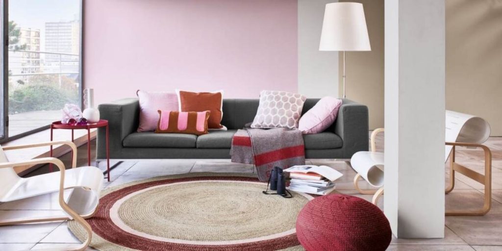 soggiorno con pareti rose, divano grigioe cuscini colorati, tappeto a forma di cerchio rosso e beige e tavolino rosso ikea