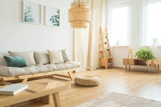 Soggiorno estivo con divano e mobili in legno chiaro e cuscini, lampadario e pouf in vimini e parquet