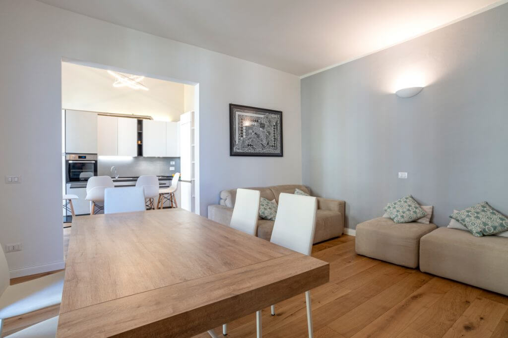 Living con divano e poltrone in velluto e tavolo in legno con sedie bianche.