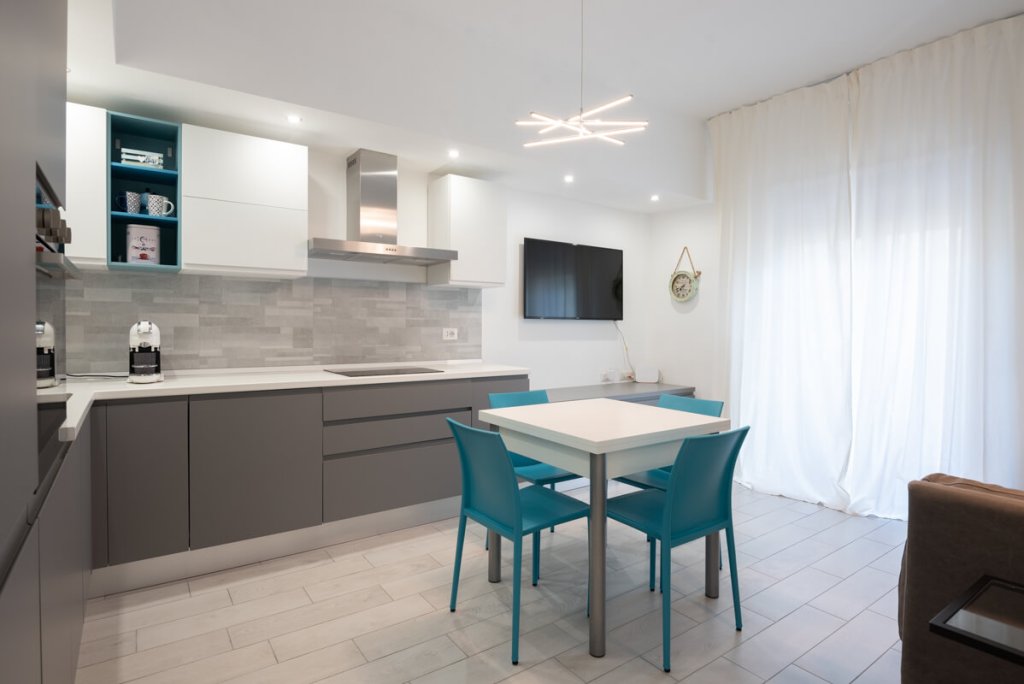 Bed and breakfast con cucina bianca e grigia e tavolo bianco con sedie azzurre.