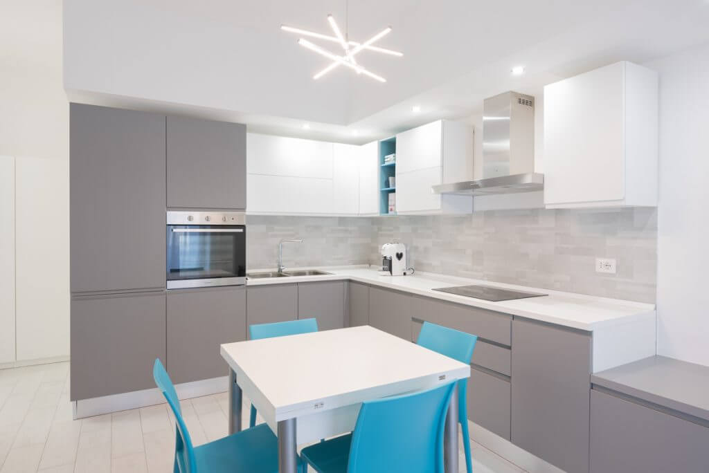 Cucina moderna con mobili bianchi e grigi e tavolo bianco con sedie azzurre.