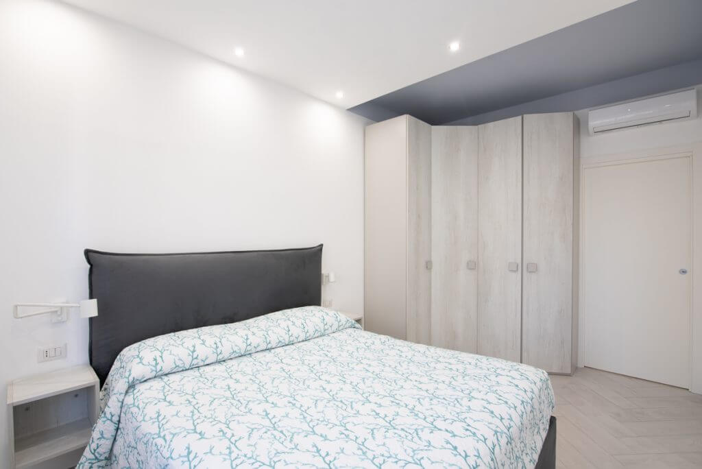 Camera matrimoniale con letto grigio e armadio angolare.