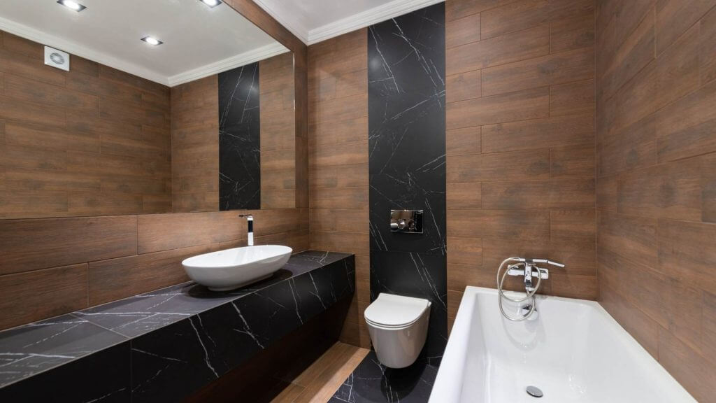 Lavabo bagno da appoggio, sospeso e da incasso: quale scegliere? | Facile Ristrutturare bagno con rivestimenti in marmo nero e legno con lavandino da appoggio bianco dalla forma ovale.