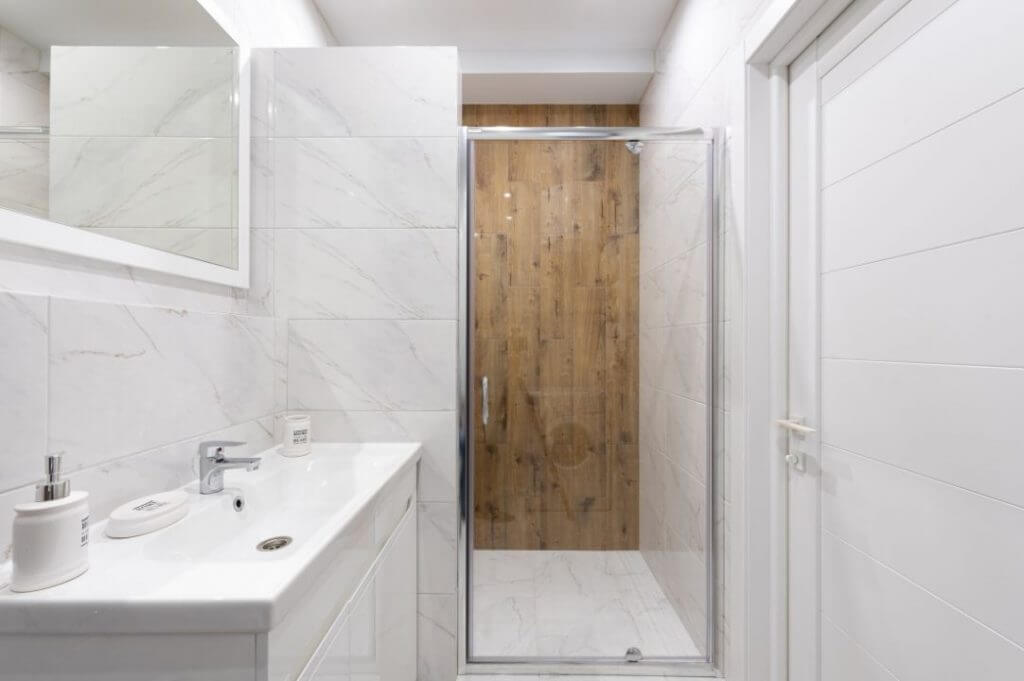 Cinque idee di ristrutturazione per il bagno piccolo | Facile Ristrutturare idee ristrutturazione bagno moderno con lavabo bianco rettangolare e rivestimenti doccia effetto legno.