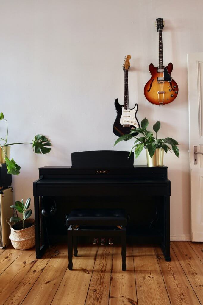angolo musica in casa con chitarre appese al muro e pianoforte