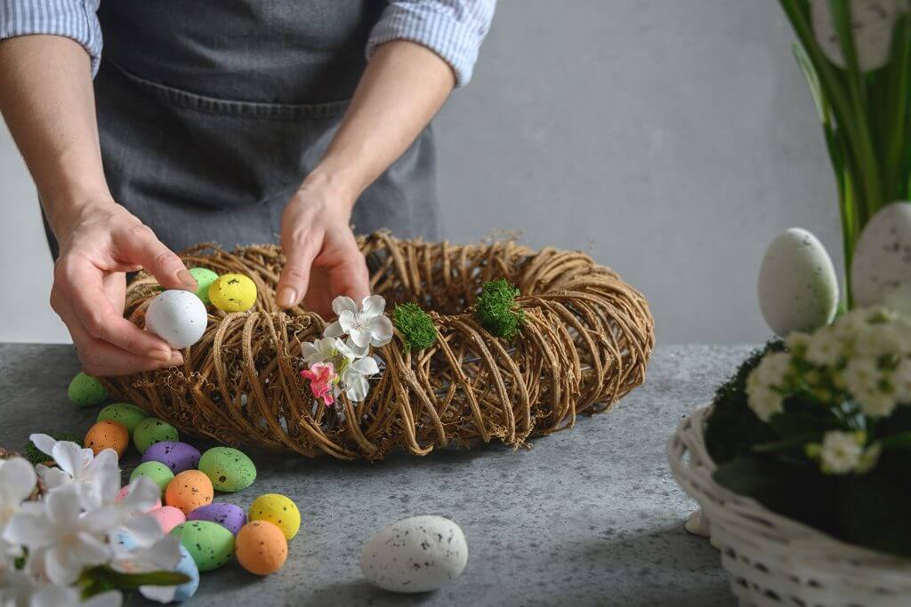 Persona che compone decorazione pasquale con uova e fiori