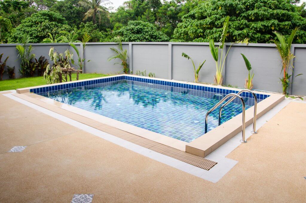 Quale piscina scegliere? Un tuffo tra i nostri consigli! | Facile Ristrutturare Piscina con piante laterali,staccionata grigia e pavimento in mattonelle marroni