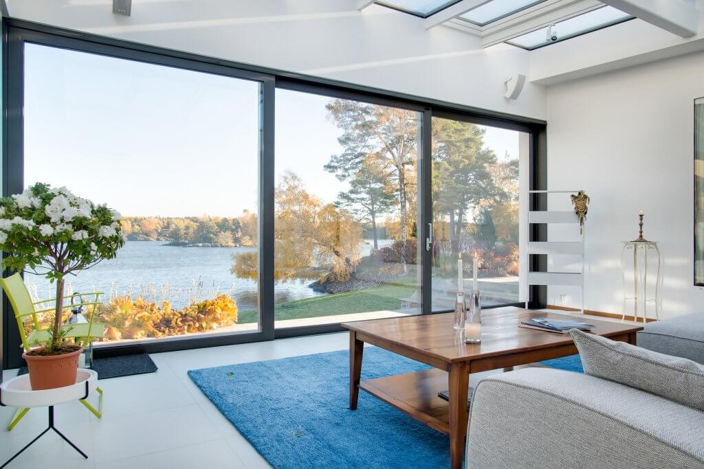 Coastal style, la nuova tendenza dell'interior design per portare il mare in casa | Facile Ristrutturare Soggiorno con tappeto azzurro, finestra laterale, divano bianco e tavolo in legno
