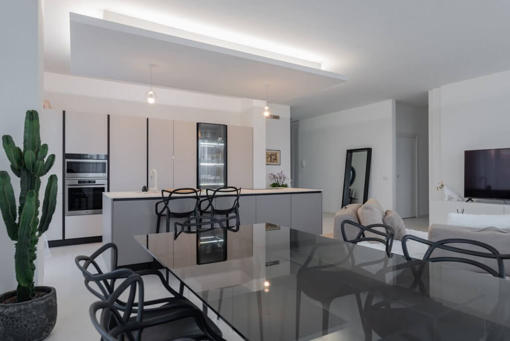 Progetto ristrutturazione Milano, open space living cucina moderno, tavolo a vetro fumè com sedie scure, cucina isola