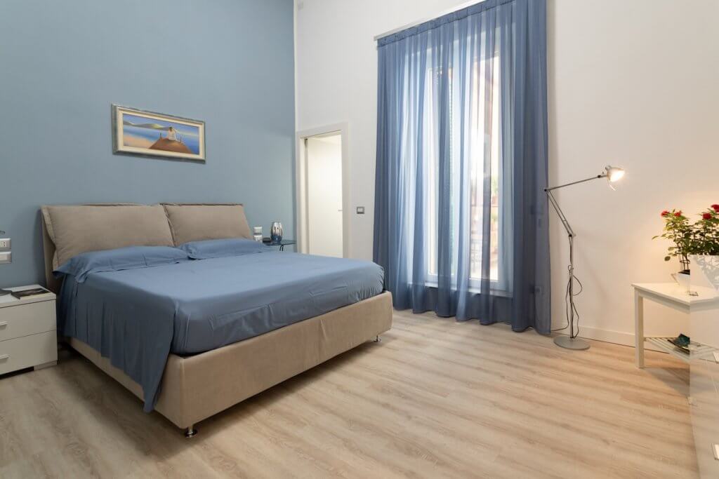 Ristrutturazione casa a Piombino, camera da letto con toni pastello e tende azzurre