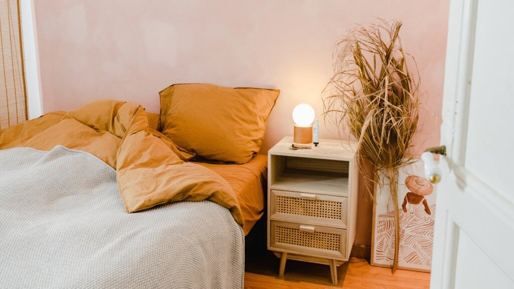 Arredare casa in stile natural chic | Facile Ristrutturare Camera da letto con cuscini, comodino in rattan con lampada e pianta laterale