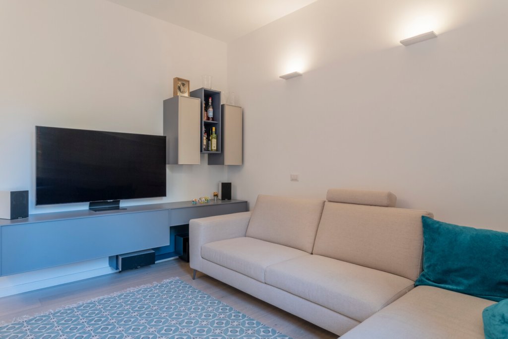 Soggiorno con divano bianco, cuscini azzurri, illuminazione, libreria