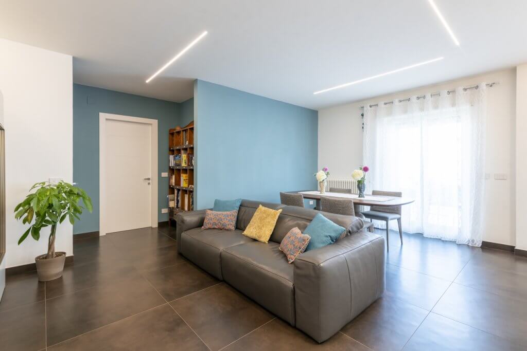 Open space con divano in pelle grigio e pavimento in Grace porcellanato effetto legno